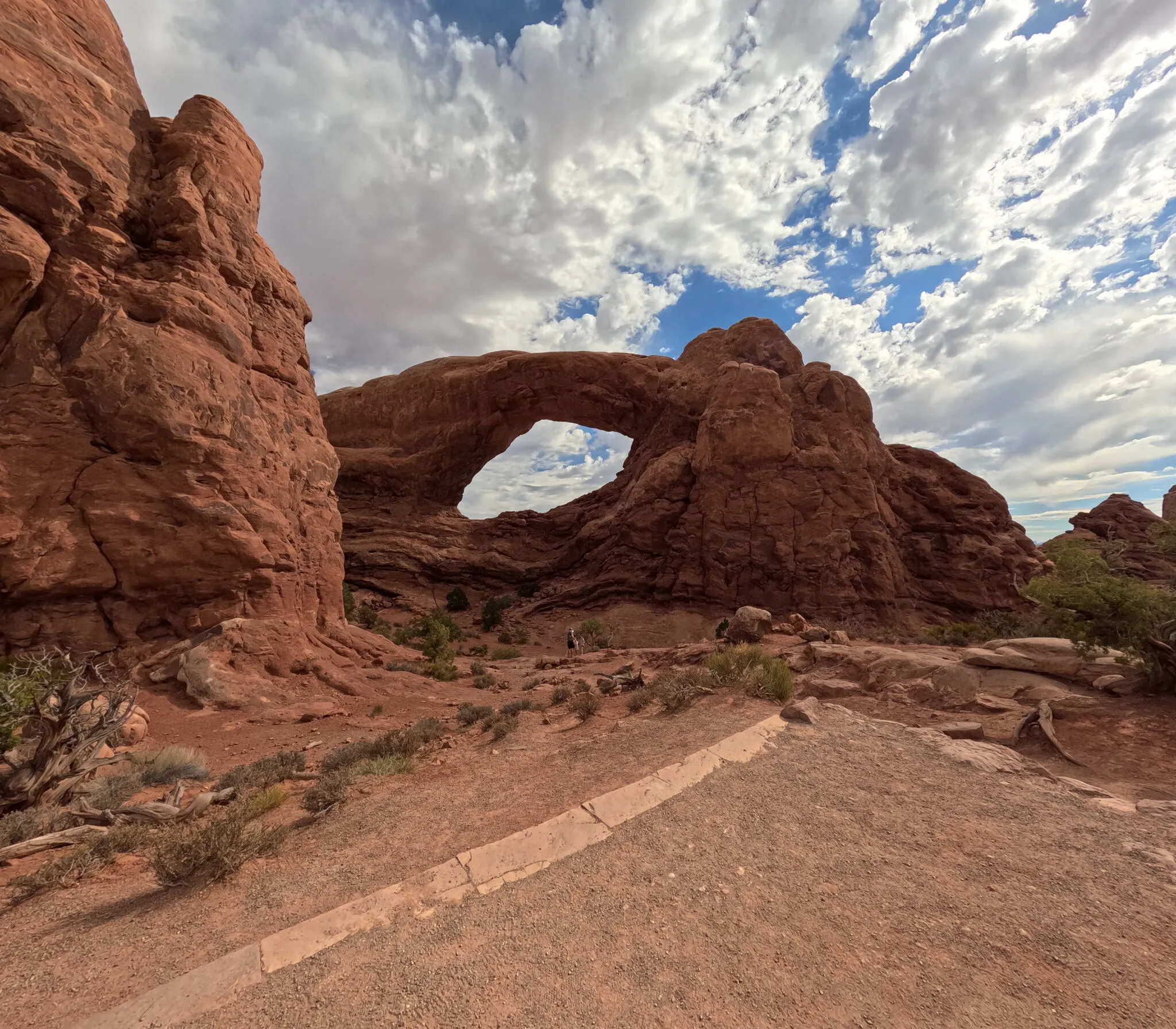 A red rock arch beneath a cloud-filled sky