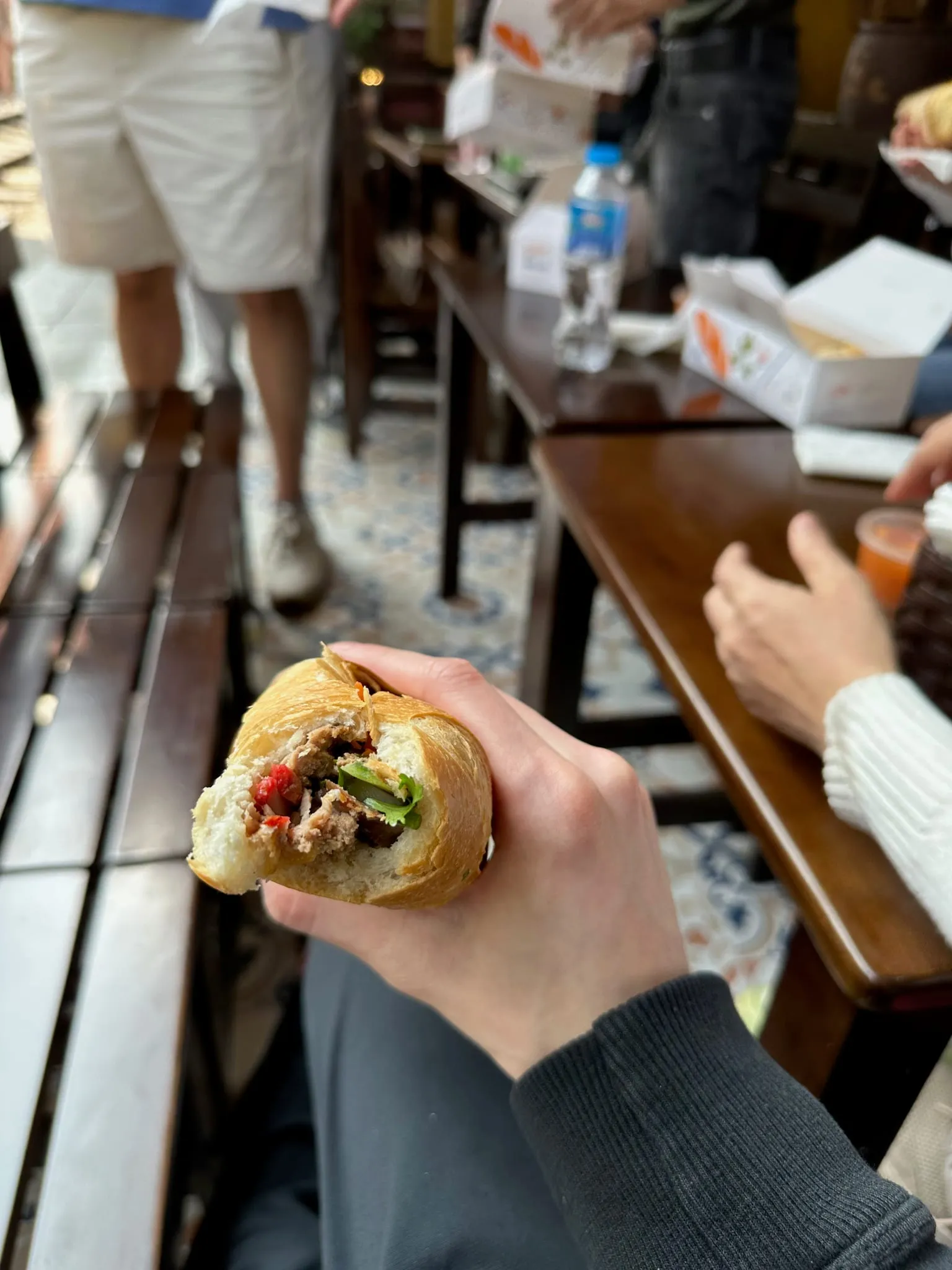 A half-eaten banh mi held over a café table