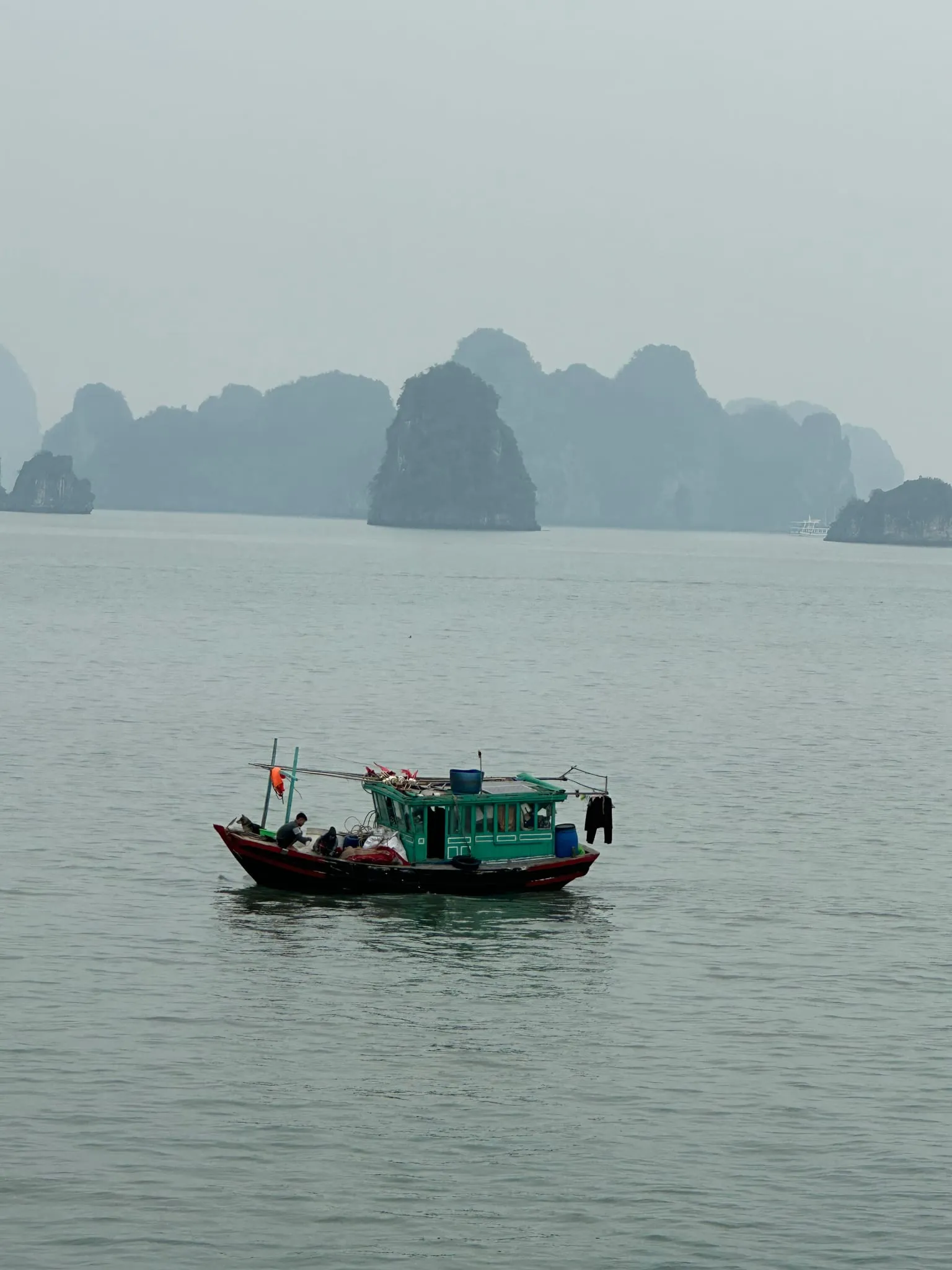 A small fishing boat in front of limestone islands in Ha Long Bay